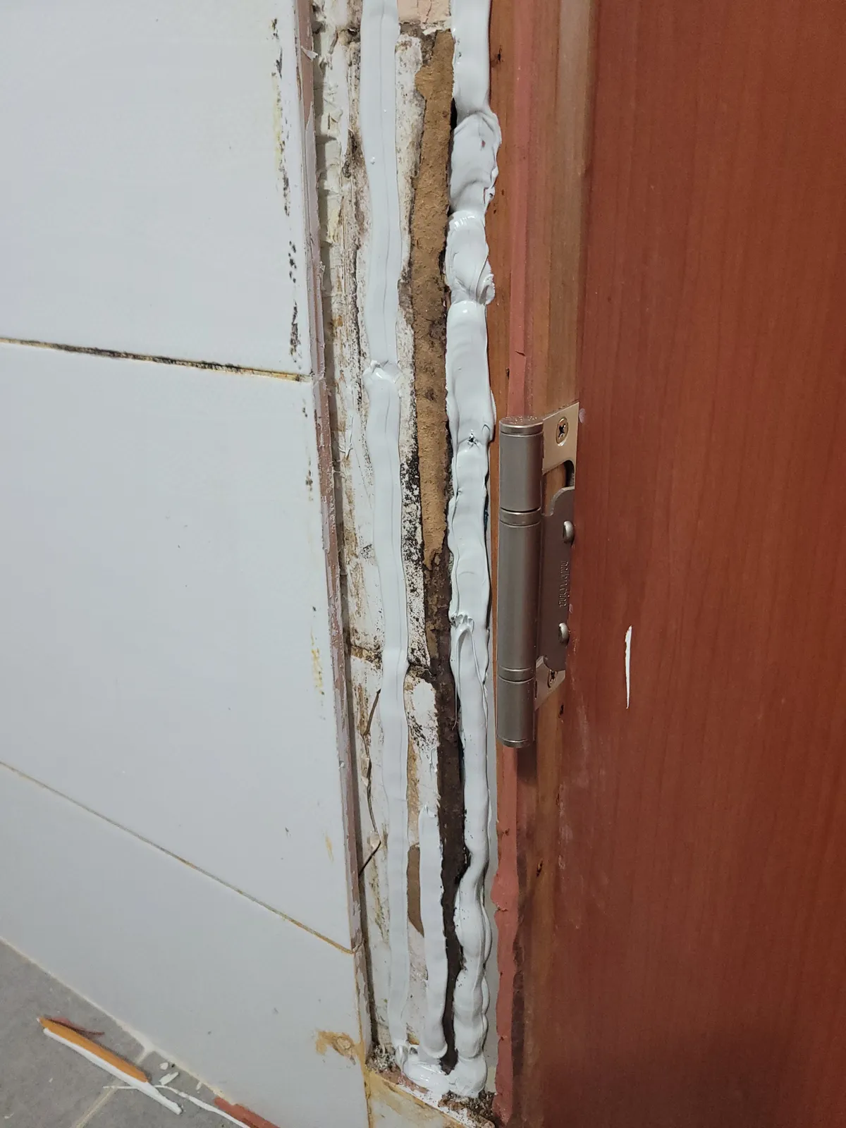 문틀을 뜯어낸 자리에서 경첩 주변이 부식되고 실리콘과 접착 흔적이 남아 있는 작업 중 모습