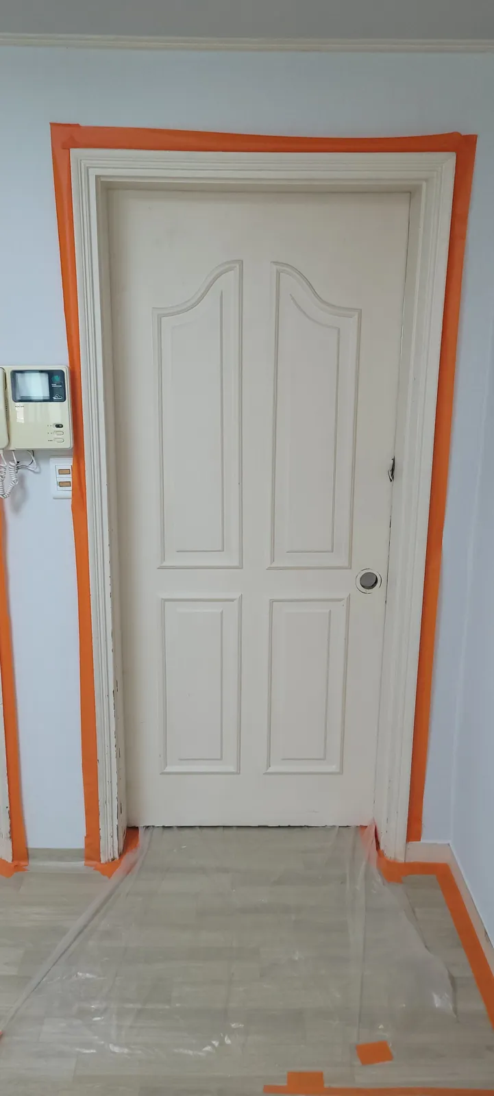 문틀 주변을 주황색 테이프로 마스킹하고 바닥을 덮어 도색 중인 현장